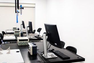 Laboratório de eletrônica com computadores, monitores e equipamentos técnicos sobre bancadas.