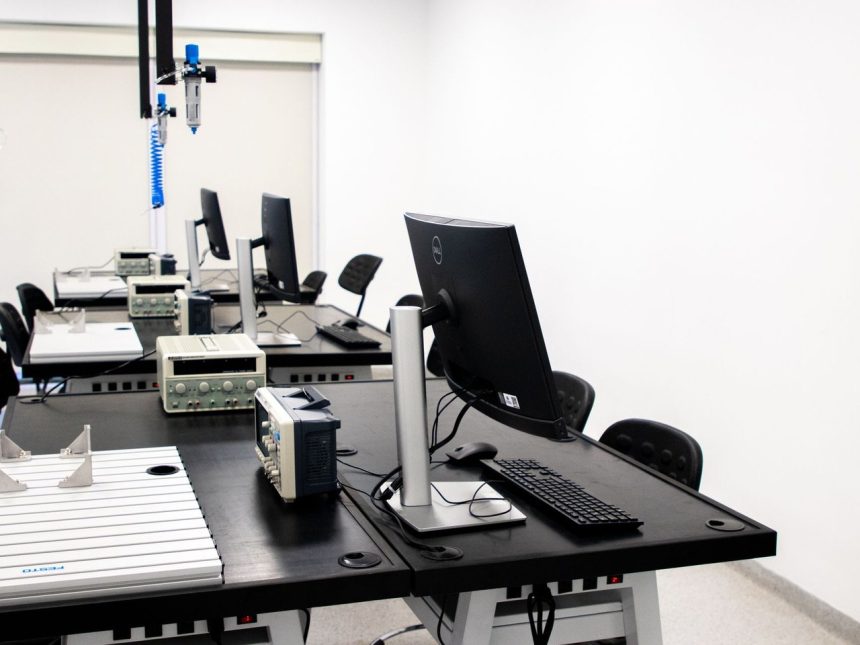 Laboratório de eletrônica com computadores, monitores e equipamentos técnicos sobre bancadas.