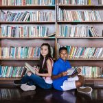Duas crianças leem livros em uma biblioteca escolar.