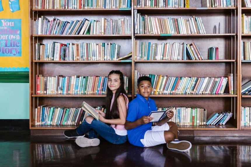 Duas crianças leem livros em uma biblioteca escolar.