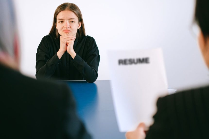 Mulher participa de entrevista de emprego diante de dois recrutadores, com o currículo sobre a mesa.