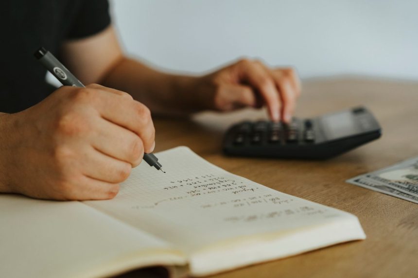 Mãos fazem cálculos em um caderno ao lado de uma calculadora, representando planejamento financeiro.