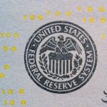 Detalhe do selo do Federal Reserve sobre uma cédula americana, com números digitais amarelos sobrepostos.