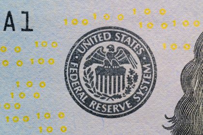 Detalhe do selo do Federal Reserve sobre uma cédula americana, com números digitais amarelos sobrepostos.